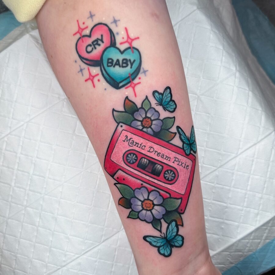 This tattoo features a retro cassette tape in a striking pink hue, surrounded by beautiful flowers and fluttering butterflies.