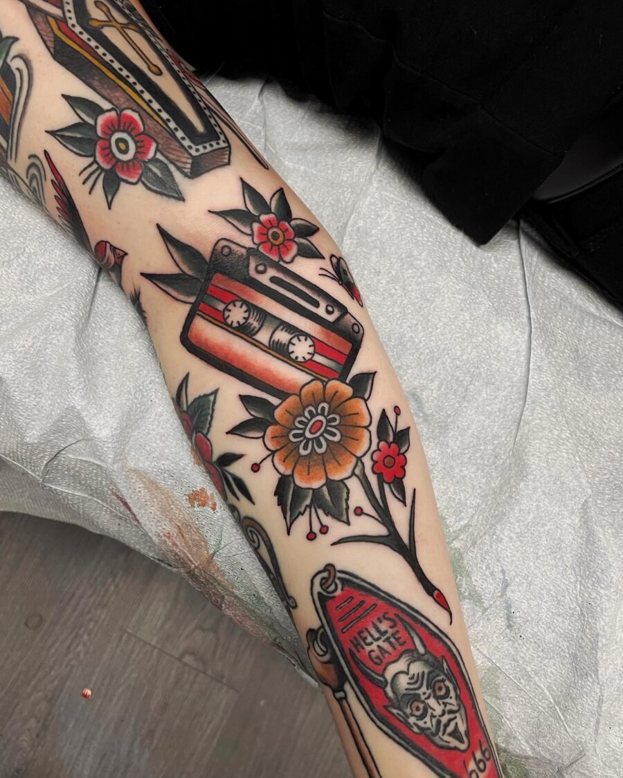 This tattoo showcases a cassette tape inked among whimsical flowers.