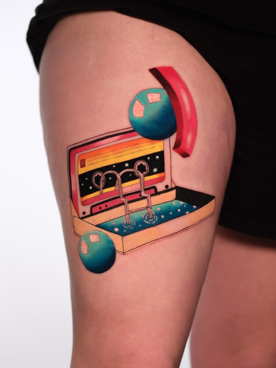 This tattoo showcases a cassette tape emerging from a box, reminiscent of nostalgic 80s aesthetics.
