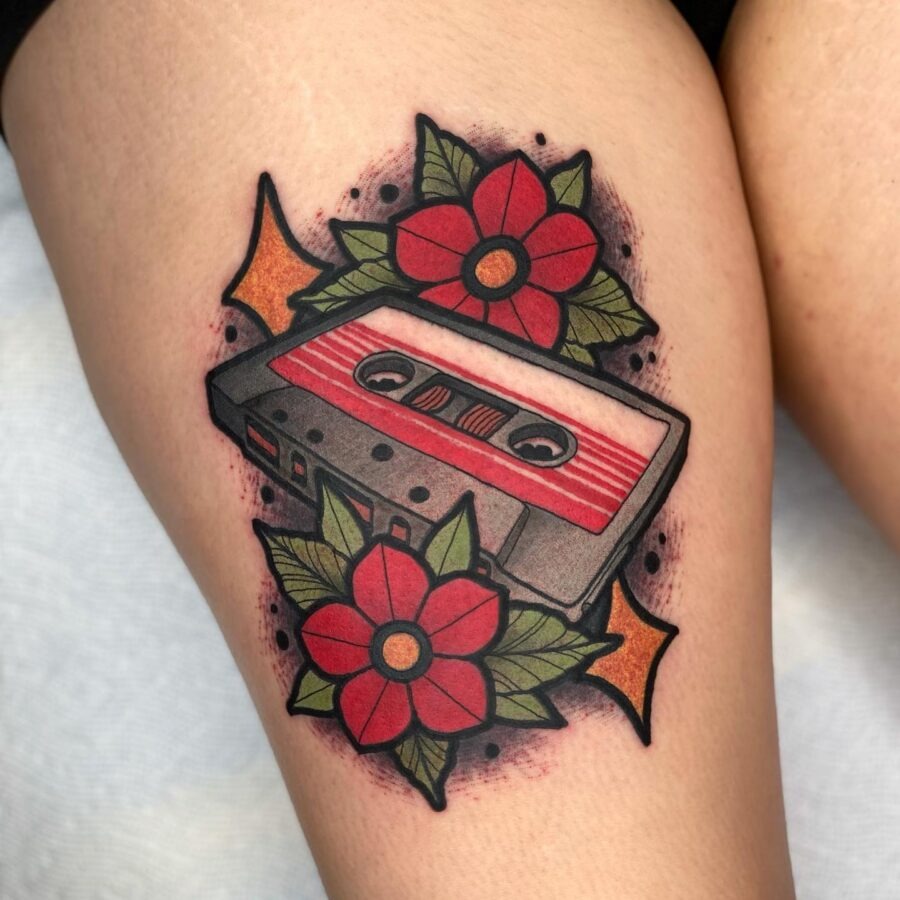 This tattoo showcases a cassette tape surrounded by blooming red flowers, creating a lively and nostalgic vibe.