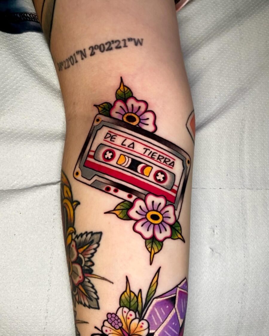This cassette tape tattoo showcases a classic design with flowers surrounding it.