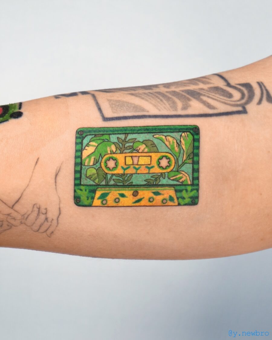 This tattoo features a retro cassette tape adorned with intricate green plant designs.