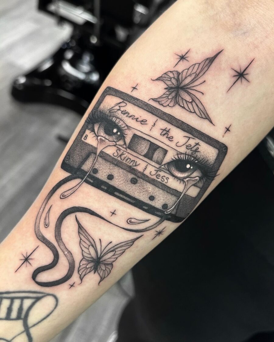 This tattoo features a classic cassette tape adorned with expressive eyes and delicate butterflies.