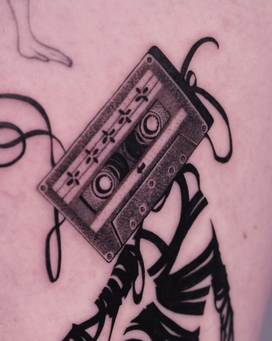 This tattoo showcases a vintage cassette tape inked in stunning detail.