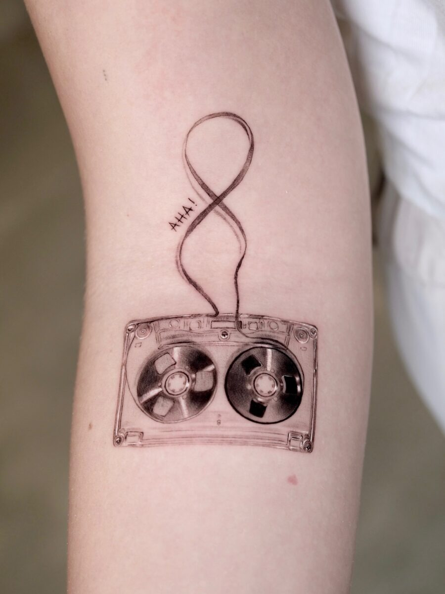 This tattoo showcases a classic cassette tape, intricately designed with an infinity loop.