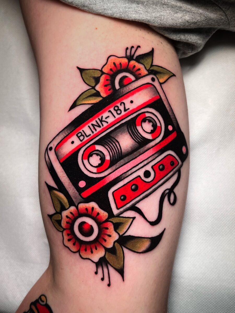 This tattoo features a classic cassette tape adorned with colorful floral elements.