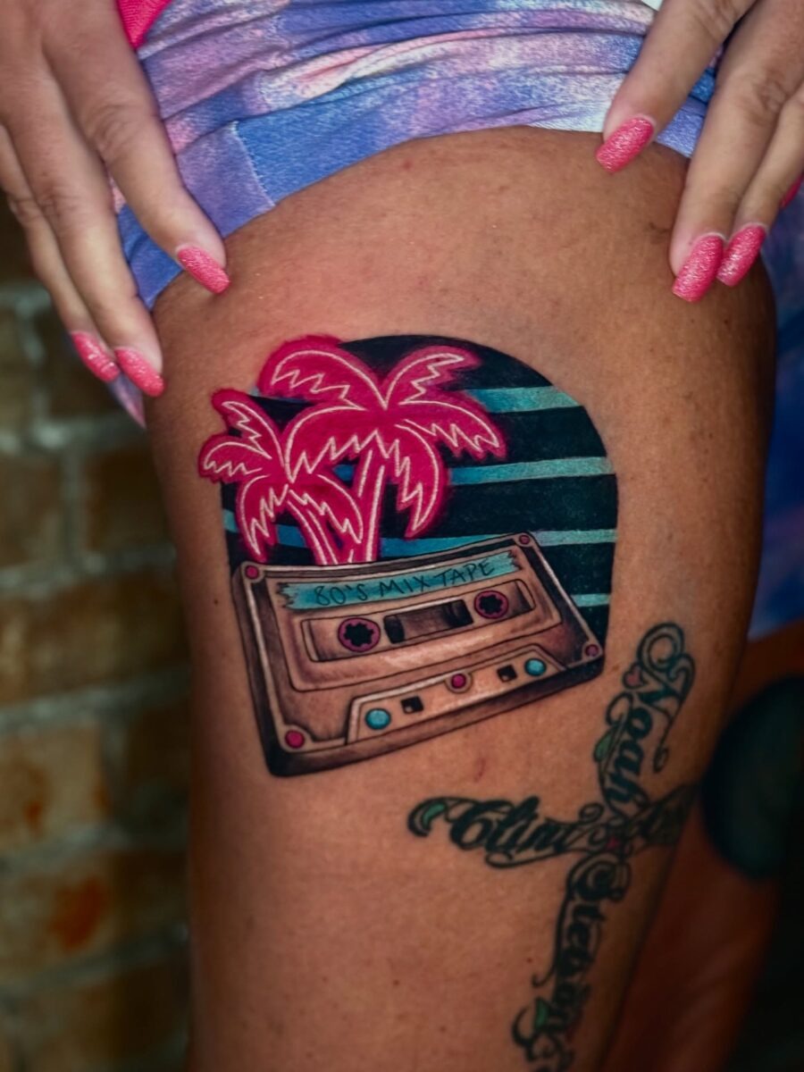 This tattoo features a colorful cassette tape adorned with palm trees, evoking a laid-back, nostalgic feel.