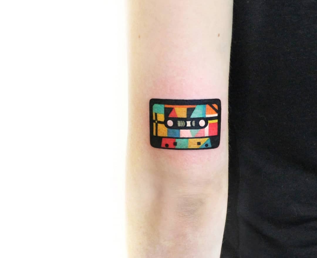 This tattoo features a colorful, geometric cassette tape, blending nostalgia with artistic flair.