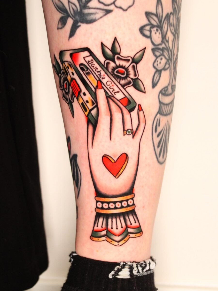 This tattoo features a beautifully detailed hand gripping a vintage cassette tape, showing a nostalgic vibe.