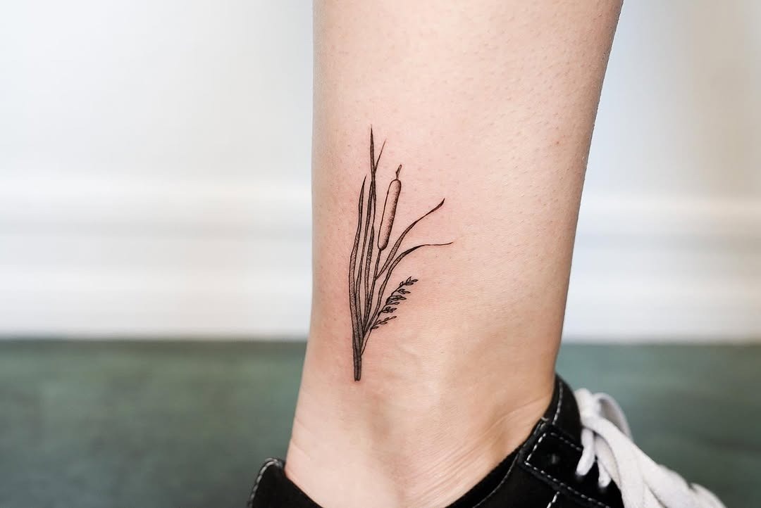 This minimalistic cattail tattoo beautifully graces the ankle, featuring delicate black ink that captures the essence of nature.