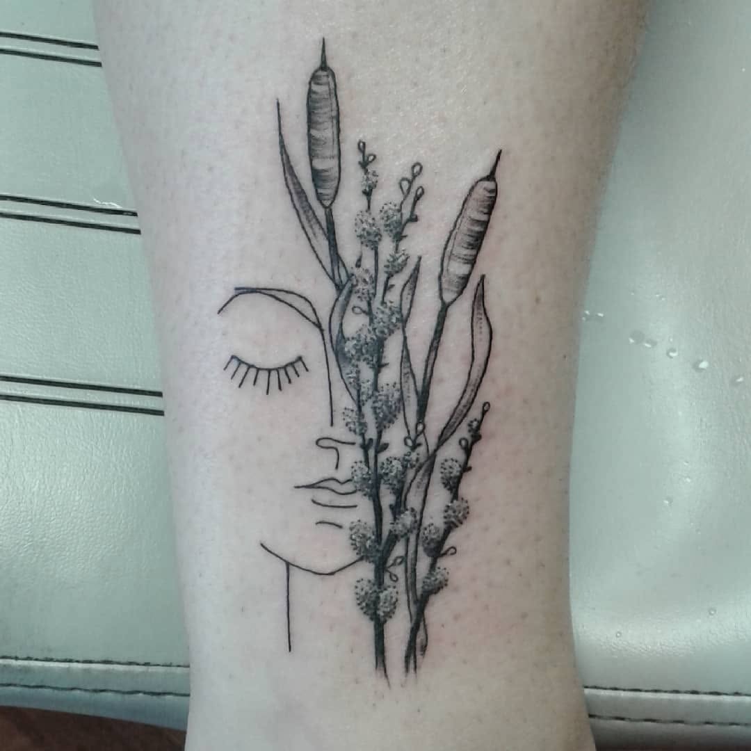 This cattail tattoo features a minimalist face intertwined with slender cattails.