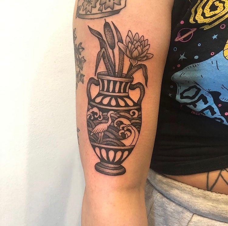 This captivating tattoo features a vase adorned with cattails and a blooming lotus.
