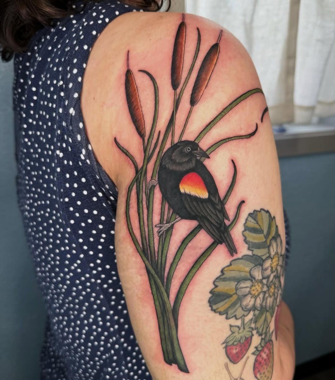 This stunning tattoo showcases a colorful bird perched among tall cattails.