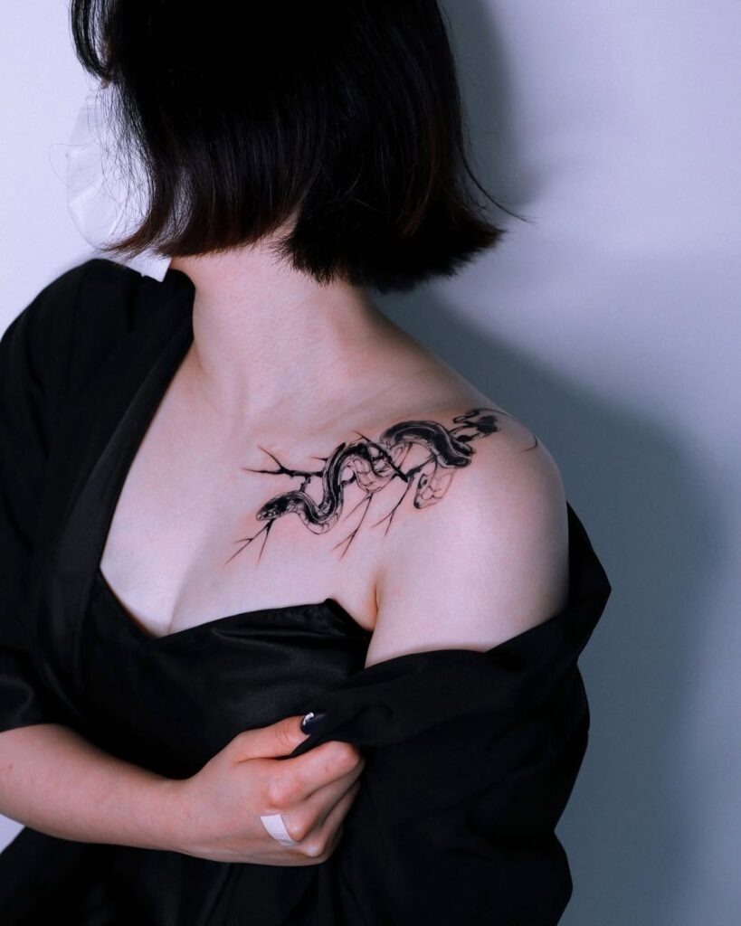 A striking collarbone tattoo featuring a coiled snake with detailed shading and bold black linework.