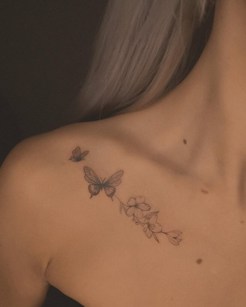 A delicate collarbone tattoo featuring elegant butterflies and soft floral elements in fine black linework.