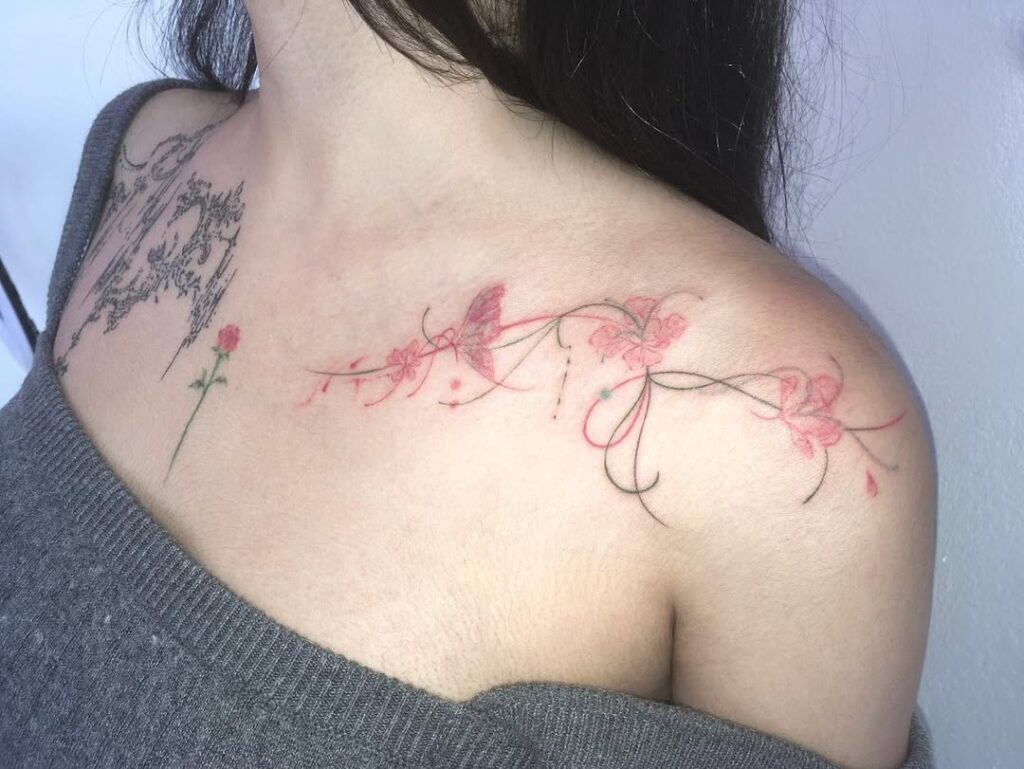 A delicate collarbone tattoo featuring pink flowers intertwined with flowing vines and a subtle butterfly.