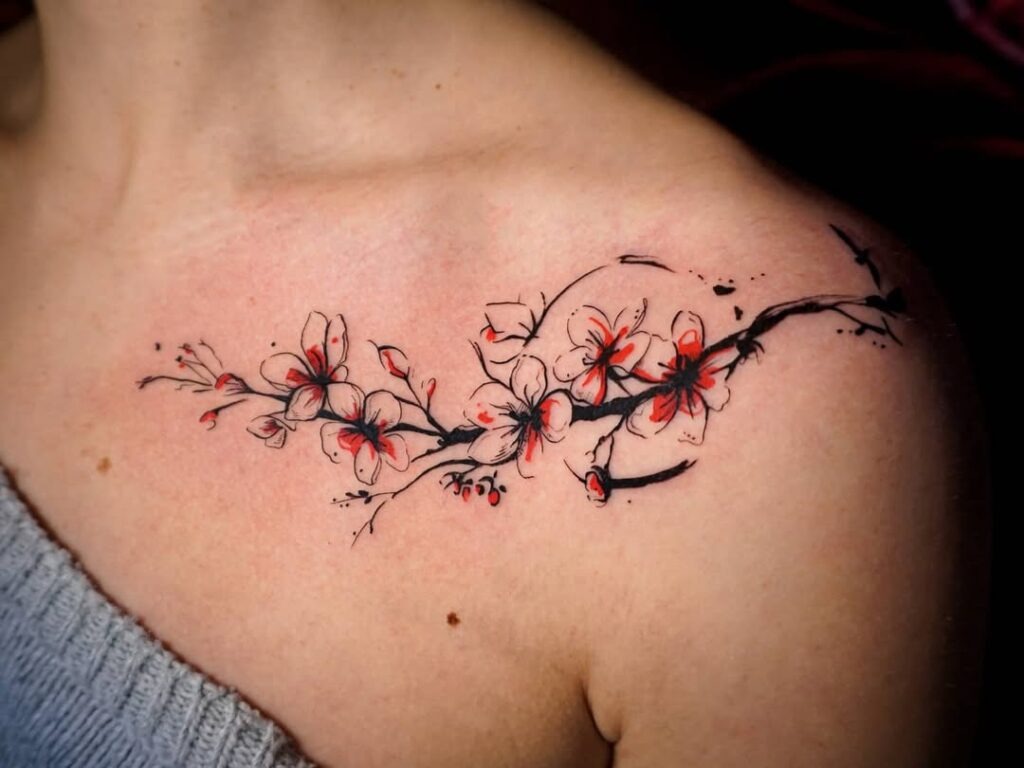 A cherry blossom tattoo spreading across the collarbone with red and black accents.
