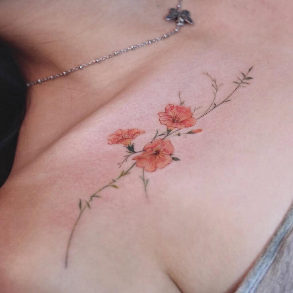 A graceful tattoo featuring orange flowers intertwined with fine, soft greenery along the collarbone.
