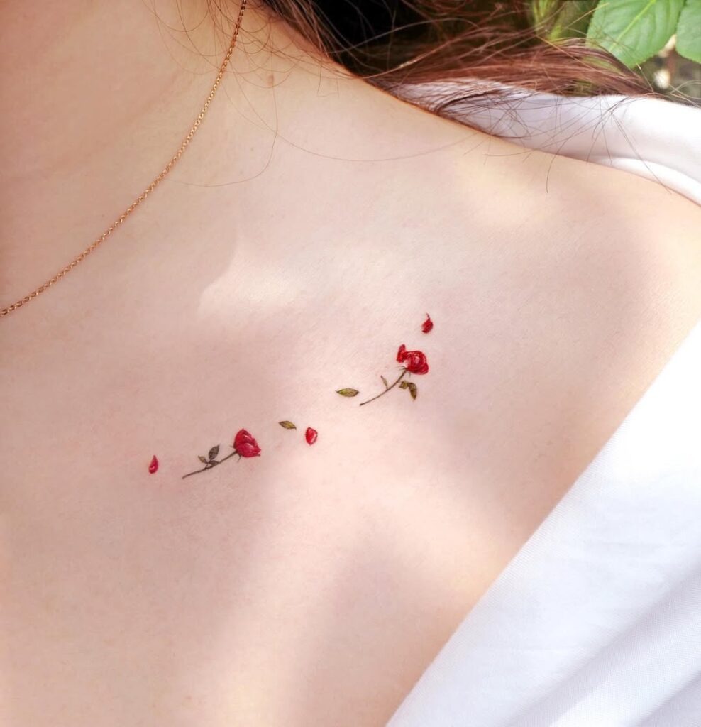 A minimalist tattoo featuring tiny red rosebuds and petals scattered gracefully along the collarbone.