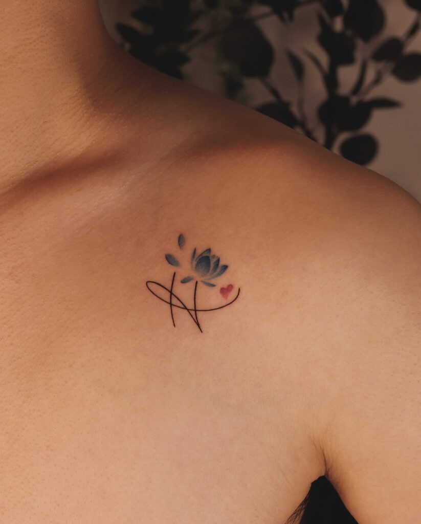 A stunning and minimalistic collarbone tattoo featuring a blue lotus flower paired with elegant linework and a tiny heart.