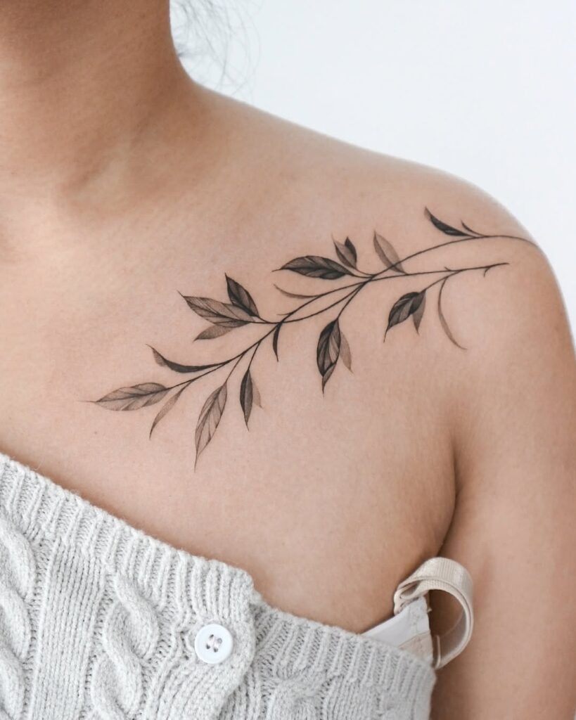 This elegant collarbone tattoo features a delicate vine with soft, detailed leaves flowing naturally along the shoulder.