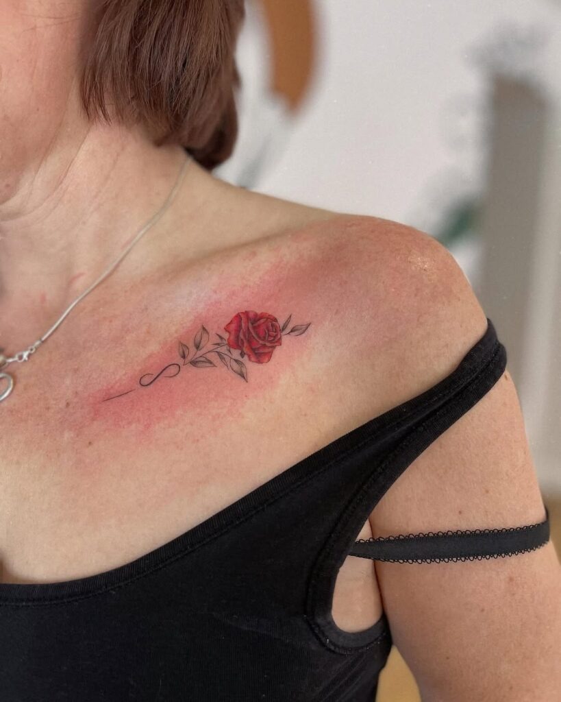 A classic red rose tattoo with delicate stems and leaves, placed gracefully along the collarbone.