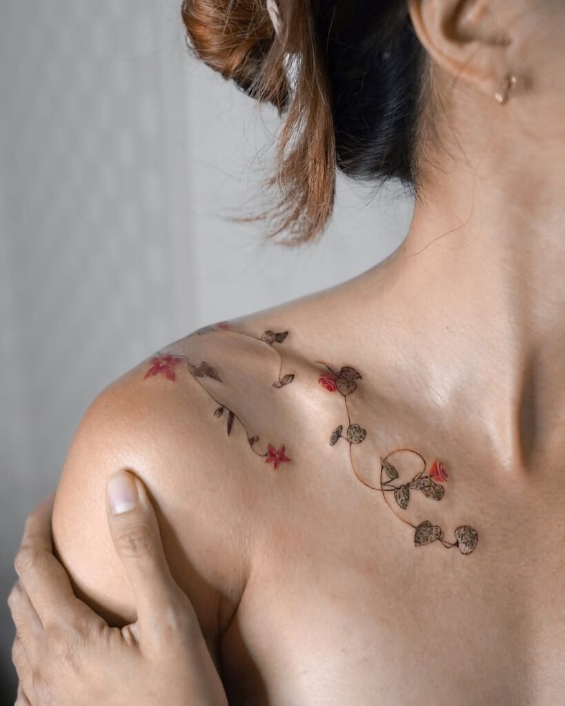 A sophisticated collarbone tattoo showing delicate vines intertwined with subtle red flowers.