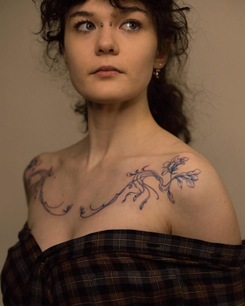 A unique collarbone tattoo with elegant blue floral stems and flowing linework.