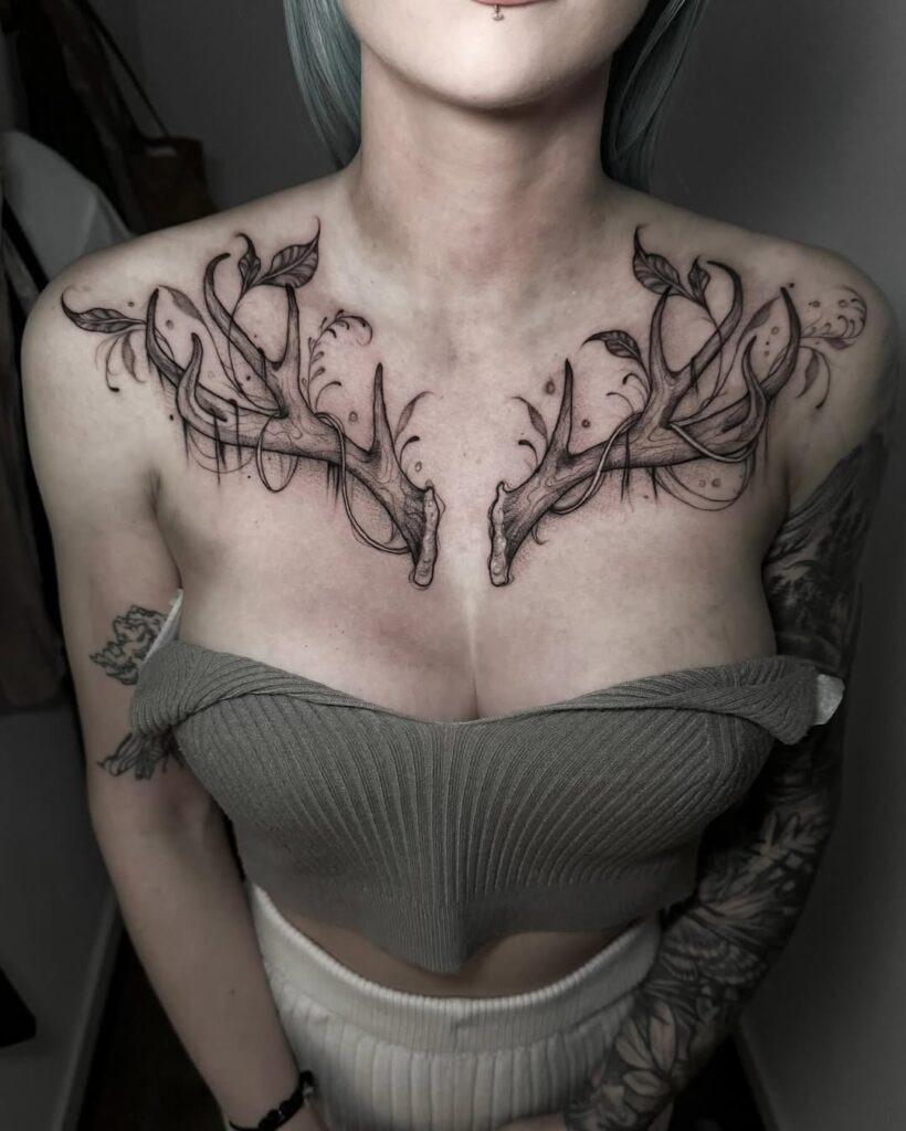 A bold and intricate collarbone tattoo featuring antler-like designs intertwined with leaves and elegant details.