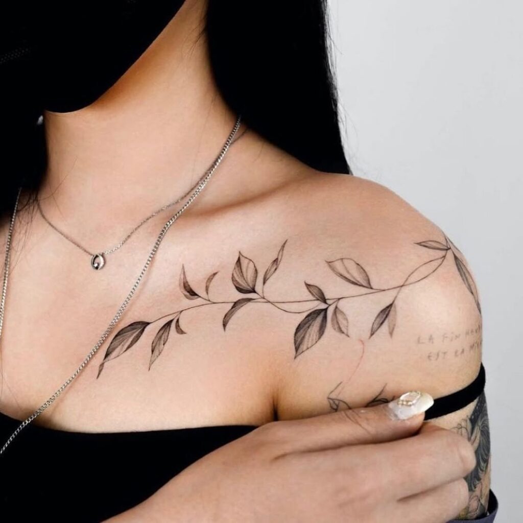 An elegant leafy vine tattoo that gracefully wraps along the collarbone with delicate black and grey details.