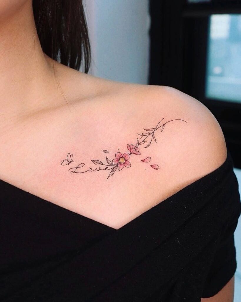 A charming collarbone tattoo featuring delicate pink flowers, falling petals, and the word "Love" in elegant script.