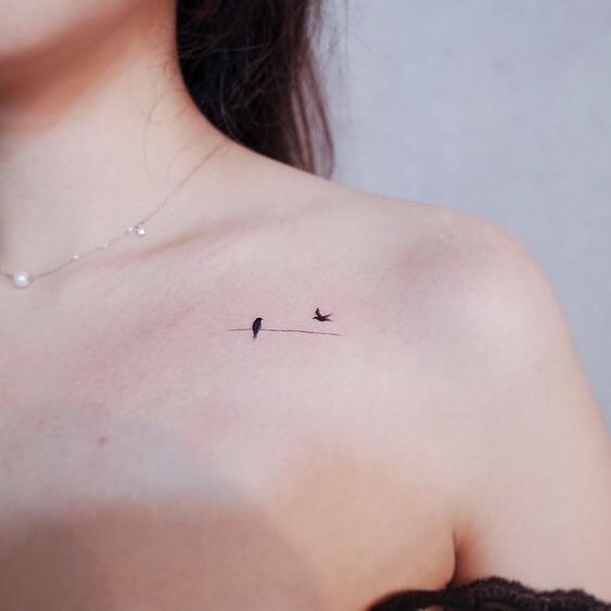 A delicate collarbone tattoo featuring two tiny birds on a thin line.
