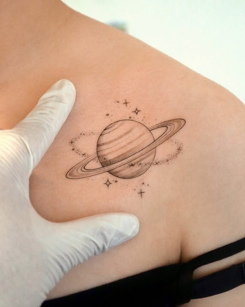 A beautifully minimalist tattoo of Saturn surrounded by delicate stars and subtle cosmic details.