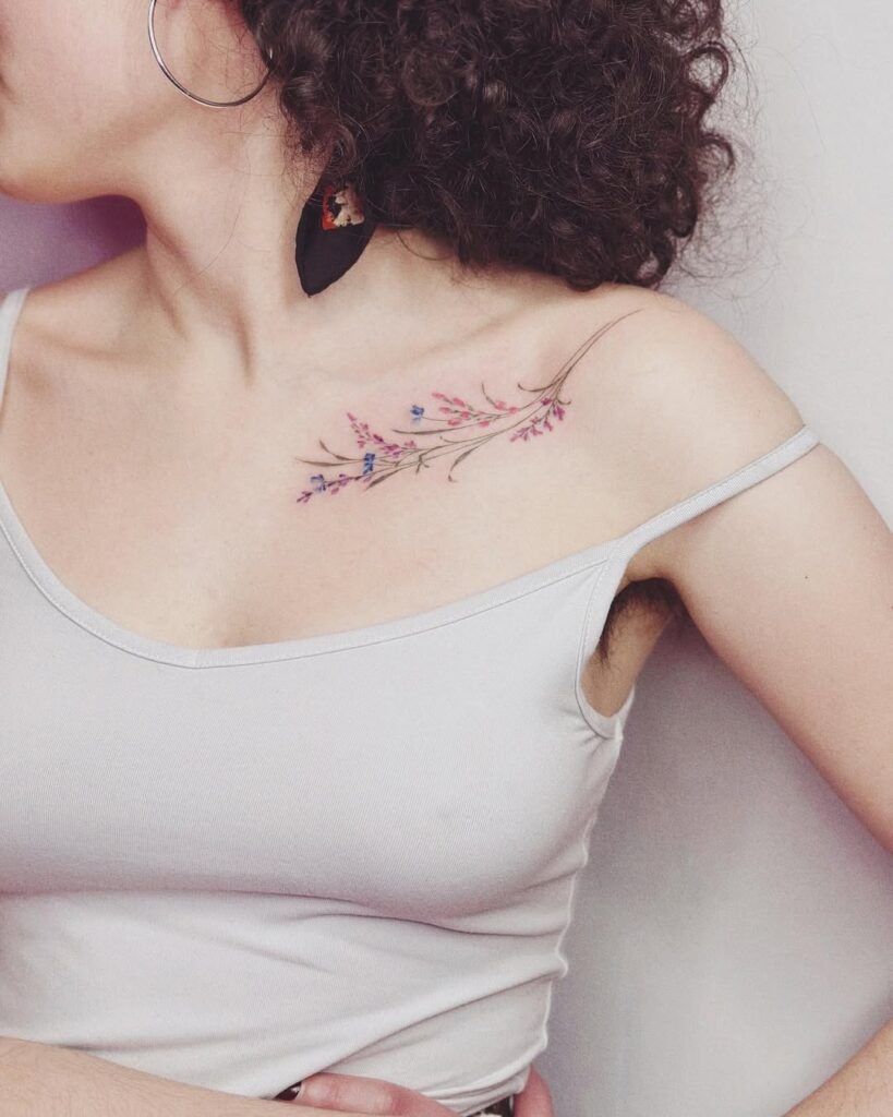 A delicate tattoo featuring soft pastel flowers and branches beautifully spread along the collarbone.