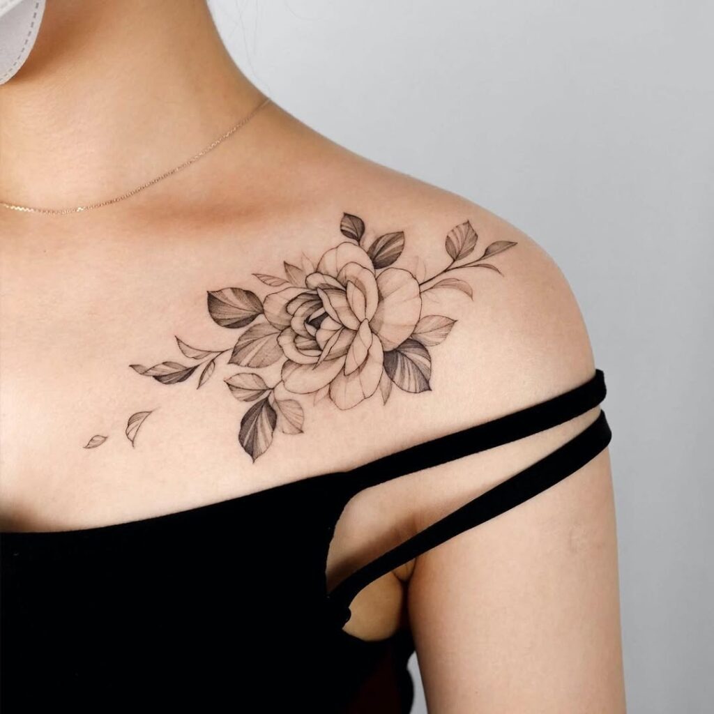 A beautifully detailed floral tattoo on one collarbone with soft black and grey shading.