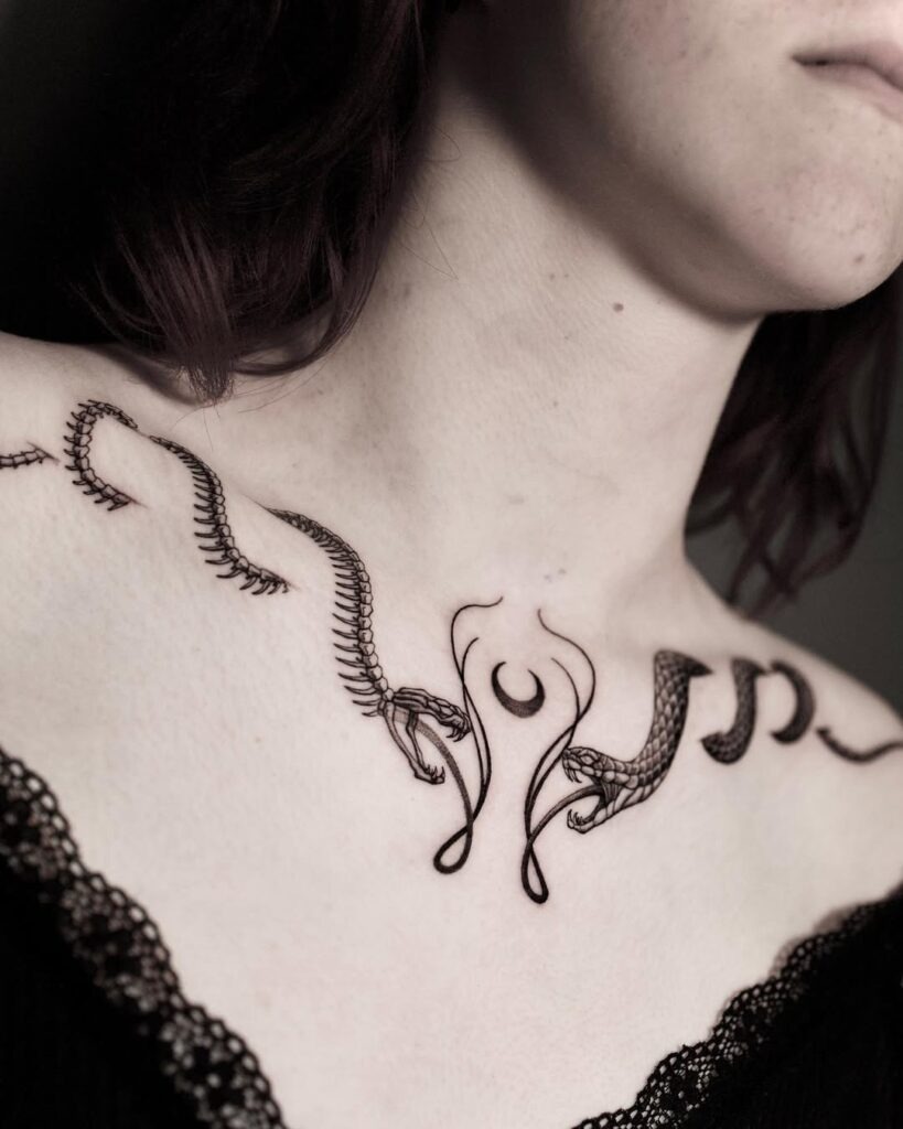 A bold collarbone tattoo featuring two snakes intertwined with intricate crescent moon and ornamental designs.