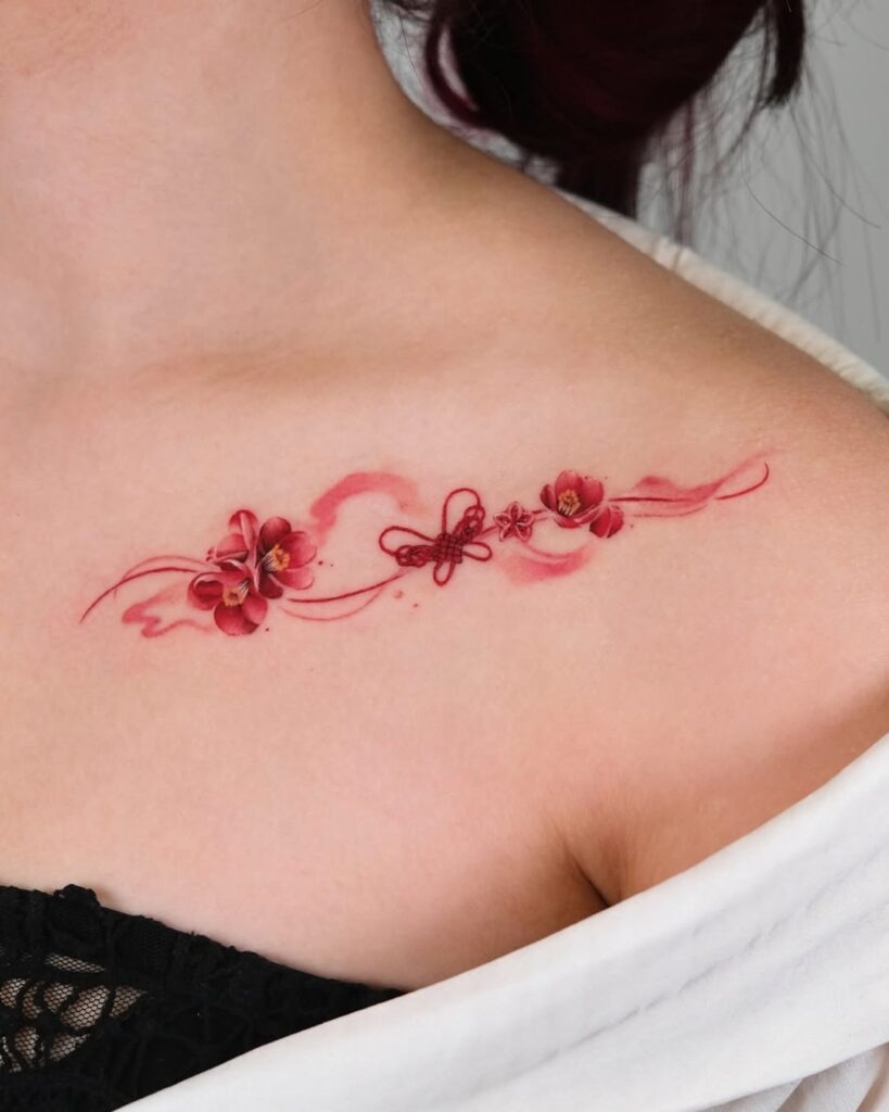 A stunning collarbone tattoo featuring bold red flowers, intricate linework, and delicate accents.
