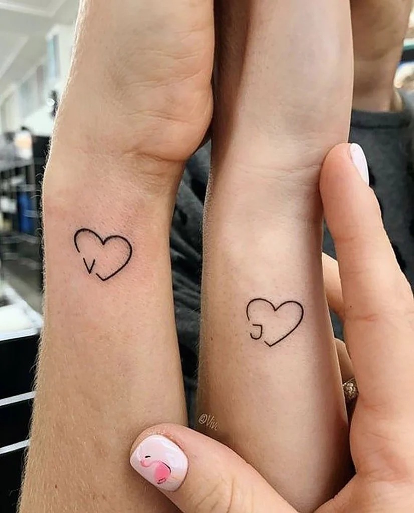 This charming tattoo design features two hearts, each with a small initial inside, representing the first letter of each partner's name.