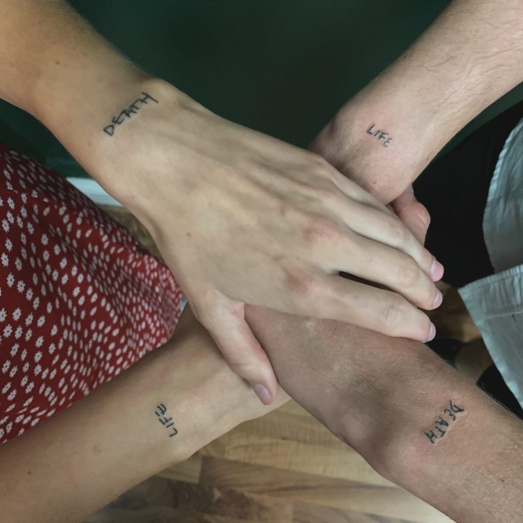This set of tattoos features the words "Life" and "Death" on the wrists of two partners.