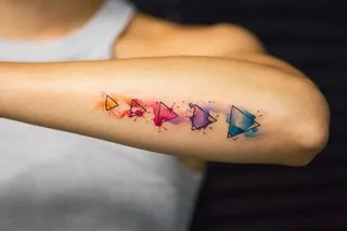 Geometric tattoos often involve precise shapes and lines, but this design disrupts the norm with its injection of watercolor effects.