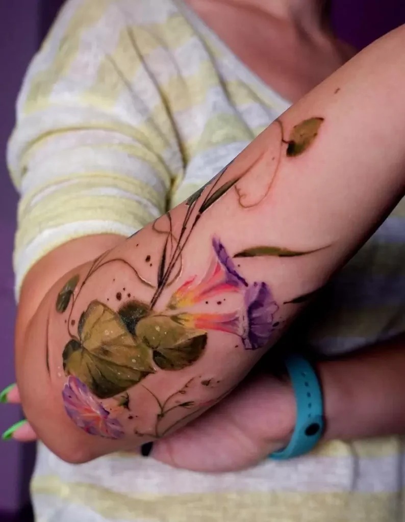 The tattoo here presents a soft, dreamlike assortment of flowers, reminiscent of a watercolor painting.