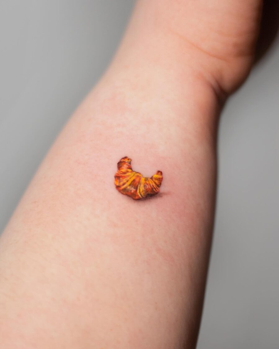 This small croissant tattoo adds a playful touch to the forearm.