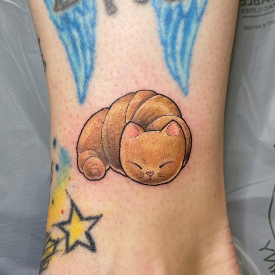 This tattoo features an adorable cat curled up, resembling a croissant.