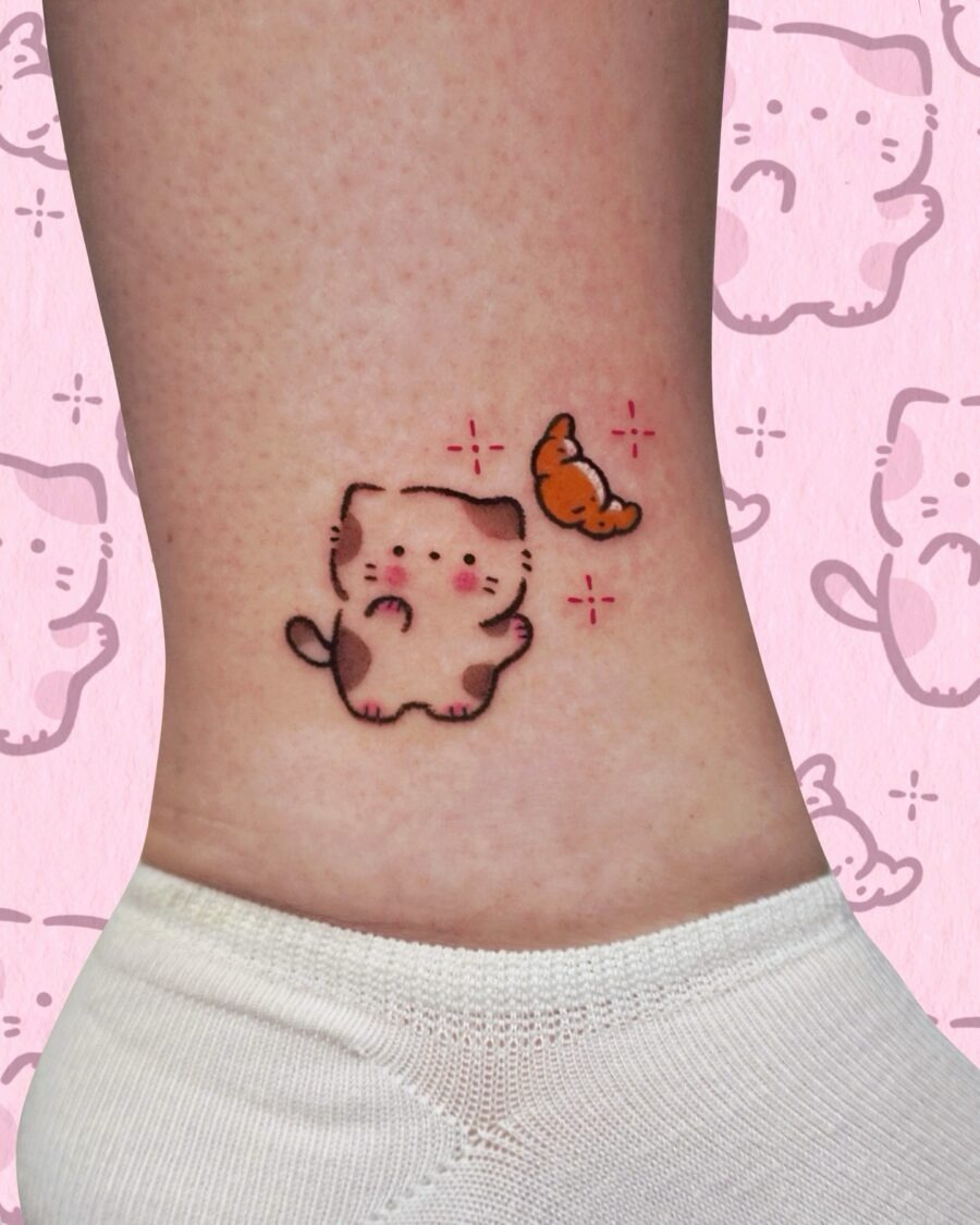 This charming tattoo features a cute cat reaching for a croissant butterfly.