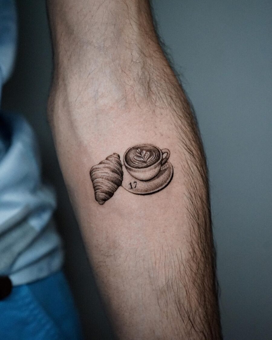This tattoo features a delectable croissant next to a beautifully crafted coffee cup.