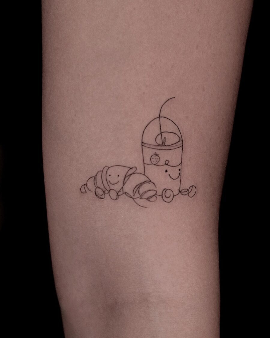 This tattoo showcases an adorable croissant paired with a cheerful drink, both exuding playful vibes.