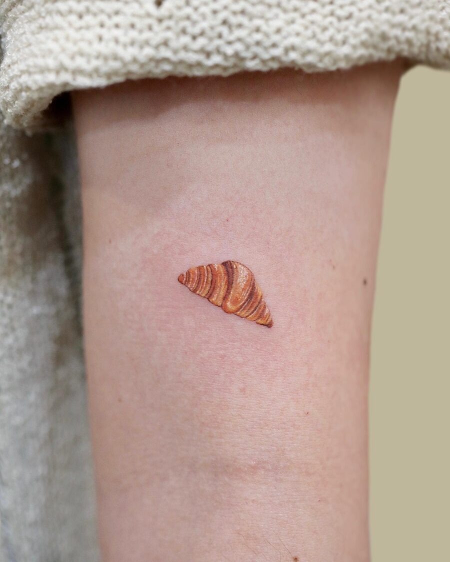 This tattoo features a beautifully detailed croissant, capturing its flaky texture and golden layers.