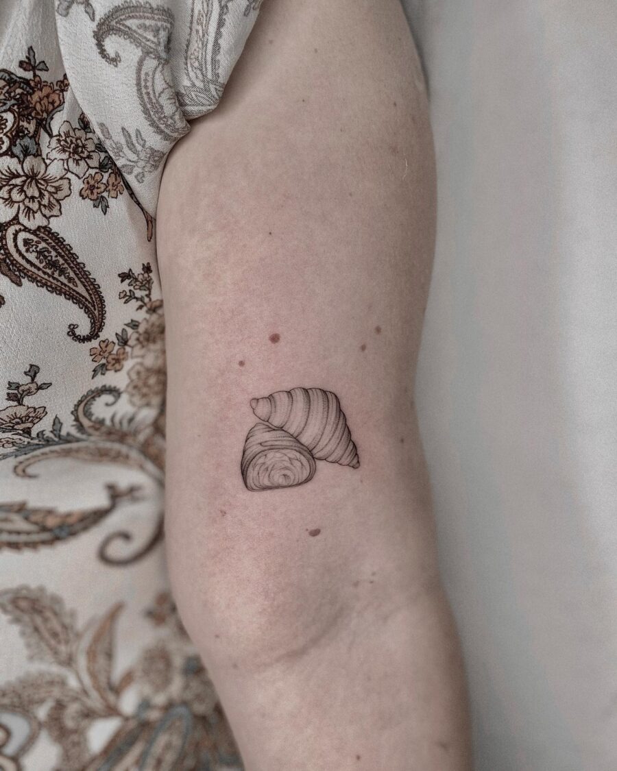 This tattoo showcases a simple yet charming croissant design inked on the arm.