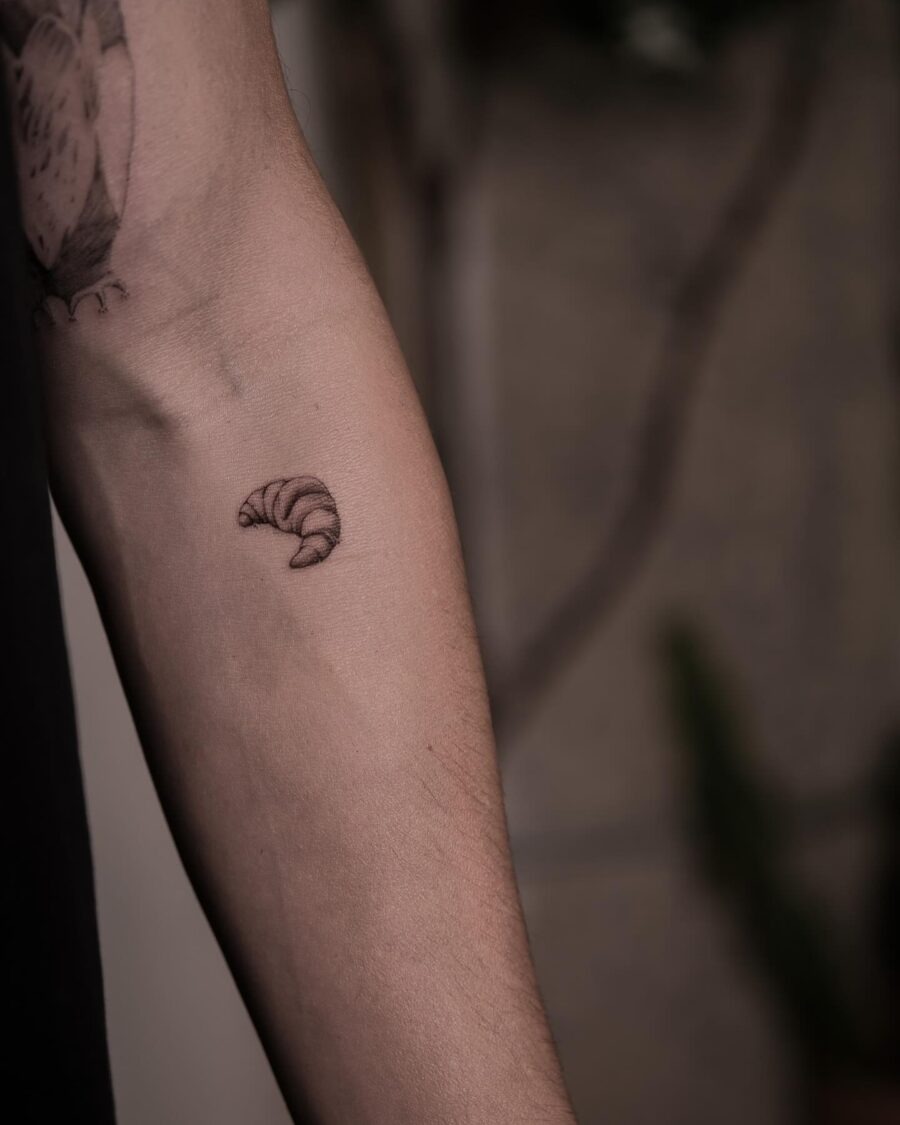 This tattoo showcases a minimalistic croissant design in fine black ink.