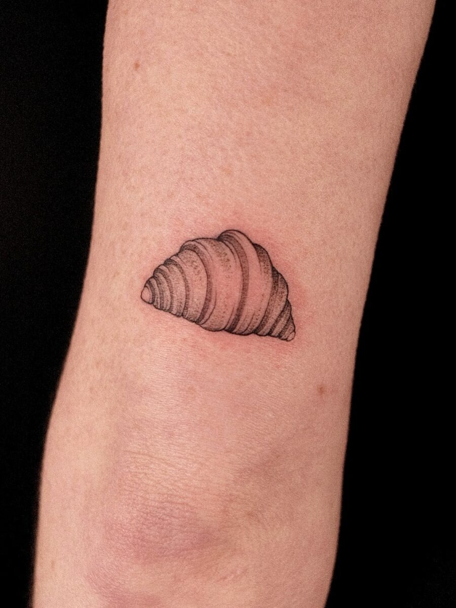 This tattoo showcases a minimalistic croissant design in fine black ink.